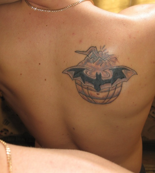 Татуировка на спине в виде летучей мыши на фоне гор и земного шара